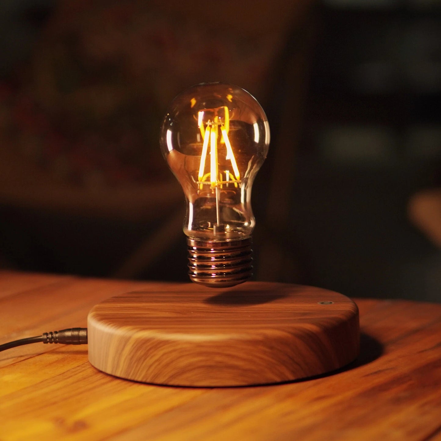 Classic light bulb magnetic levitating lamp glowing on desk with visible power cable